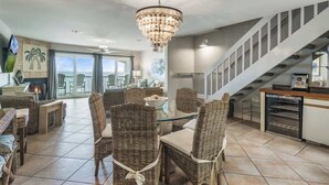 Un coin repas avec des chaises en osier et une table en verre, un lustre et un escalier.