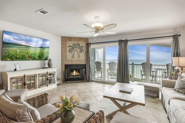 A living room with a fireplace, a television, and a view of the ocean.