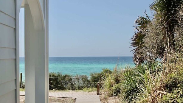 Un sentier qui mène à une plage bordée d’une eau turquoise et cristalline.