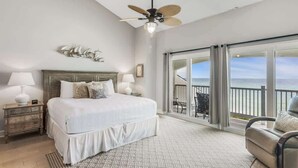 Une chambre à coucher avec un lit, des tables de chevet, un ventilateur de plafond et un balcon avec vue.