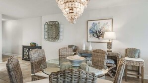 Un coin repas avec des meubles en osier, une table en verre, un lustre et un tableau abstrait encadré.