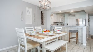 Uma cozinha moderna com armários brancos, uma mesa de jantar com cadeiras brancas e um banco.