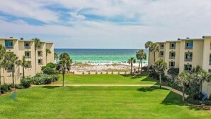 A beachfront hotel with a grassy lawn, palm trees, and a view of the ocean. - Beach-side, beautiful low-rise with uncrowded beach! (Destin)