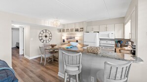 A modern kitchen with a central island, bar stools, and a large clock on the wall. - Beach-side, beautiful low-rise with uncrowded beach! (Destin)