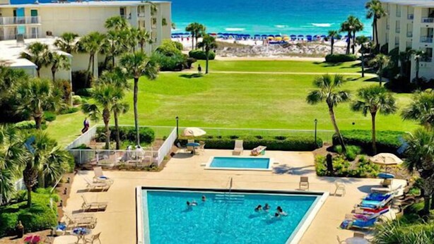 A resort with a swimming pool, beach view, and palm trees. - Beach-side, beautiful low-rise with uncrowded beach! (Destin)