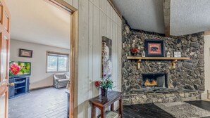 Un salon chaleureux avec une cheminée en pierre, des étagères en bois, un téléviseur et un coin salon confortable.