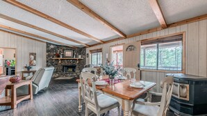 Un coin repas chaleureux avec une cheminée en pierre, des poutres en bois et une grande fenêtre donnant sur la forêt.