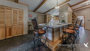 Une cuisine spacieuse avec des meubles de rangement en bois, un îlot central doté de tabourets et un luminaire suspendu.