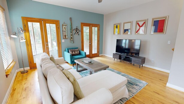 A living room with a white sofa, teal armchair, and a TV on a stand. - Coastal Vacation Paradise~ Folly Treehouse (Folly Beach)