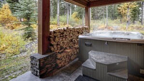 Un bain à remous avec un mur en pierre et une terrasse en bois, entouré d’une forêt.
