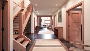 Un hall d’entrée spacieux avec un escalier en bois, un tapis et une porte donnant sur un salon.