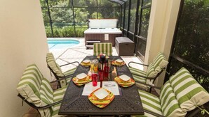 A covered patio with a table set for four, surrounded by striped cushioned chairs. A pool is visible in the background. - 6 miles to Disney: Clean Family 4 Beds, 3.5 Bath, pool/hot tub, game room, grill (Kissimmee)