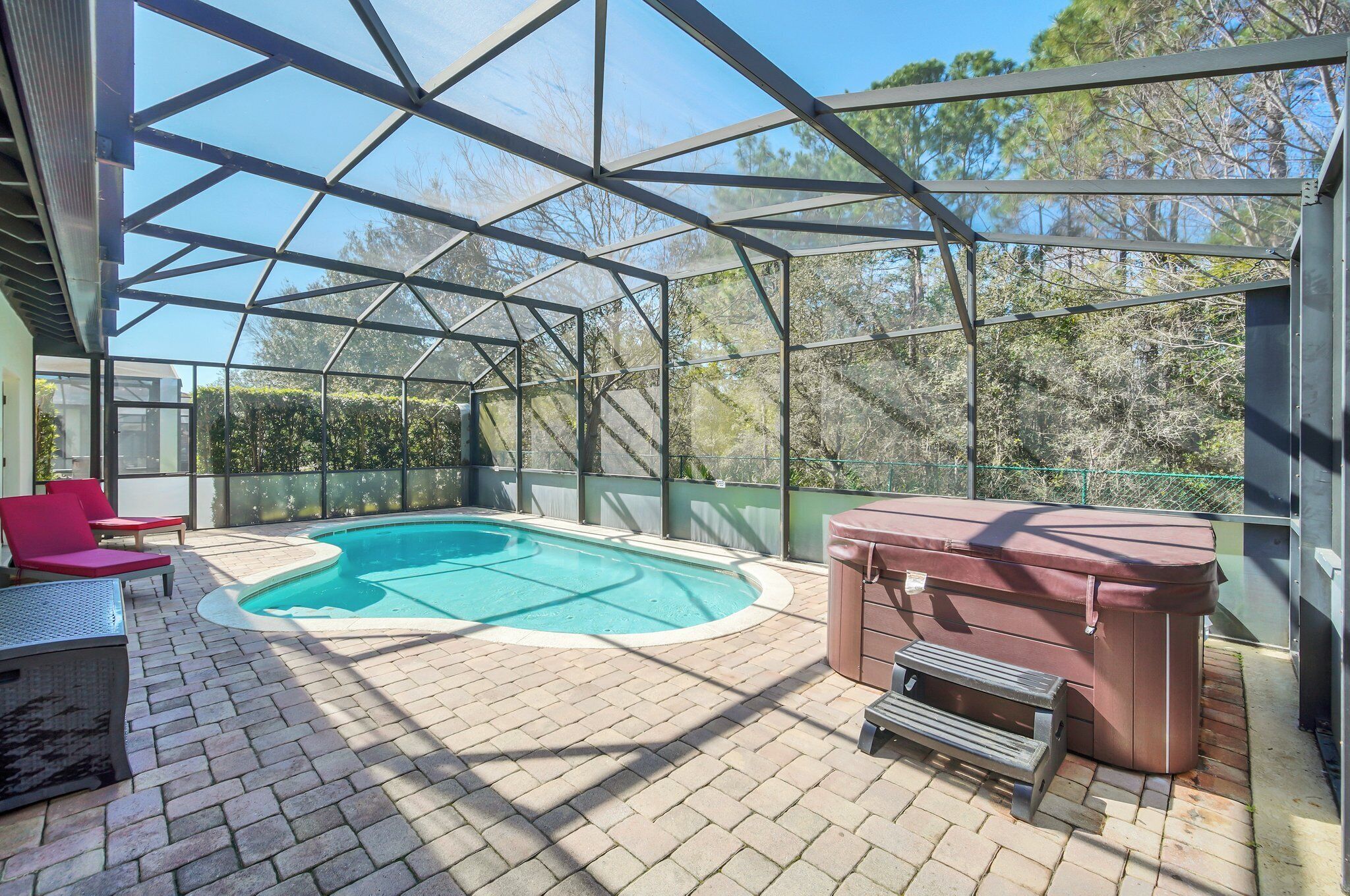 A covered outdoor swimming pool with a hot tub, seating area, and a view of trees.