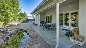 Eine überdachte Terrasse mit Gartenmöbeln, ein kleiner Teich und ein weißes Haus mit großen Fenstern.