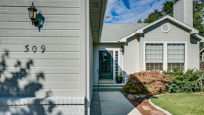 Ein Haus mit der Hausnummer 309, einer grünen Tür und einem kleinen Vorgarten mit einem Blumentopf und Sträuchern.