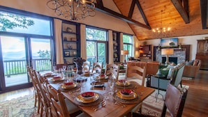 A dining area with a wooden table set for a meal, surrounded by chairs, with a view of the outdoors through large windows. - Large Mountain Home with Multi-Mile Views (Boone)