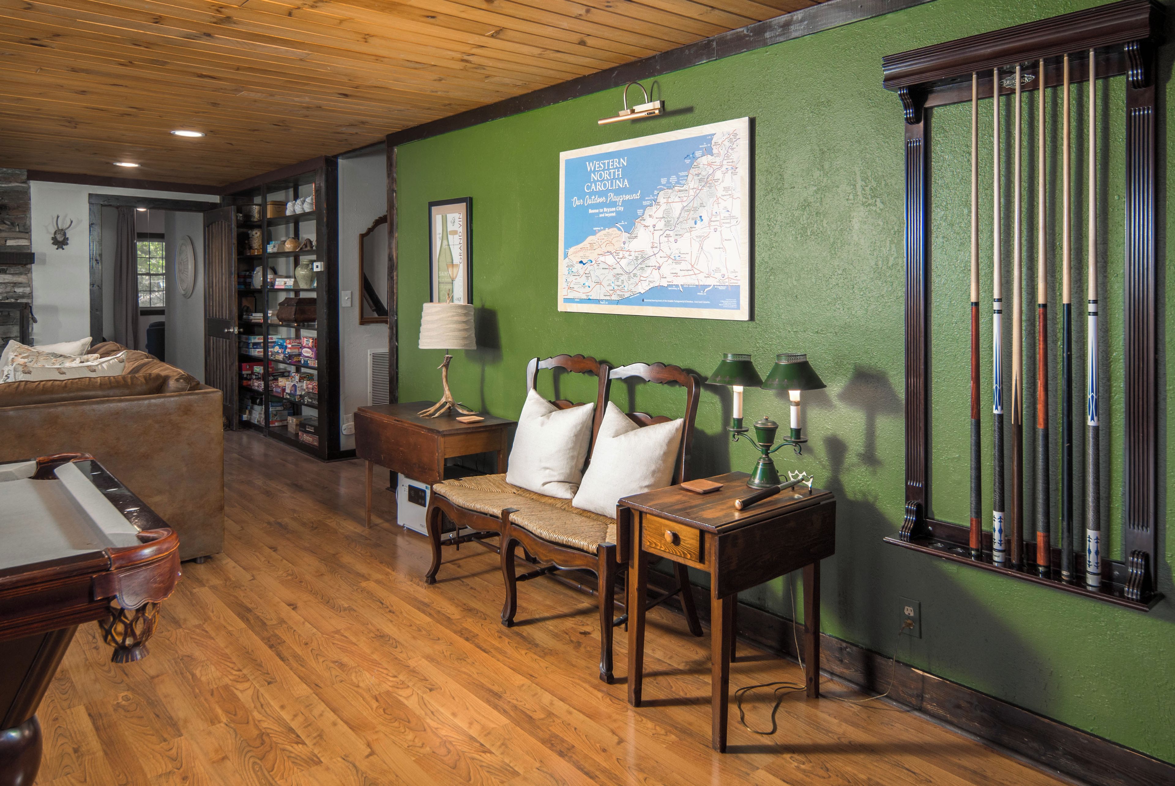 A cozy room with a wooden floor, a sofa, a map on the wall, and a billiards rack.