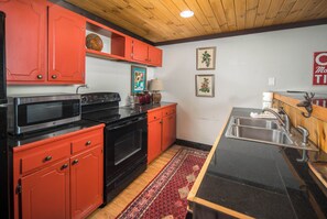 A kitchen with red cabinets, a black stove, and a stainless steel sink. - Spacious Lodge with Stunning Views, Hot Tub, Game Room & Fireplaces | Minutes to Downtown Boone (Boone)