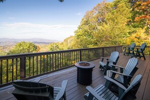 A deck with Adirondack chairs, a fire pit, and a view of a forested mountain range. - Spacious Lodge with Stunning Views, Hot Tub, Game Room & Fireplaces | Minutes to Downtown Boone (Boone)