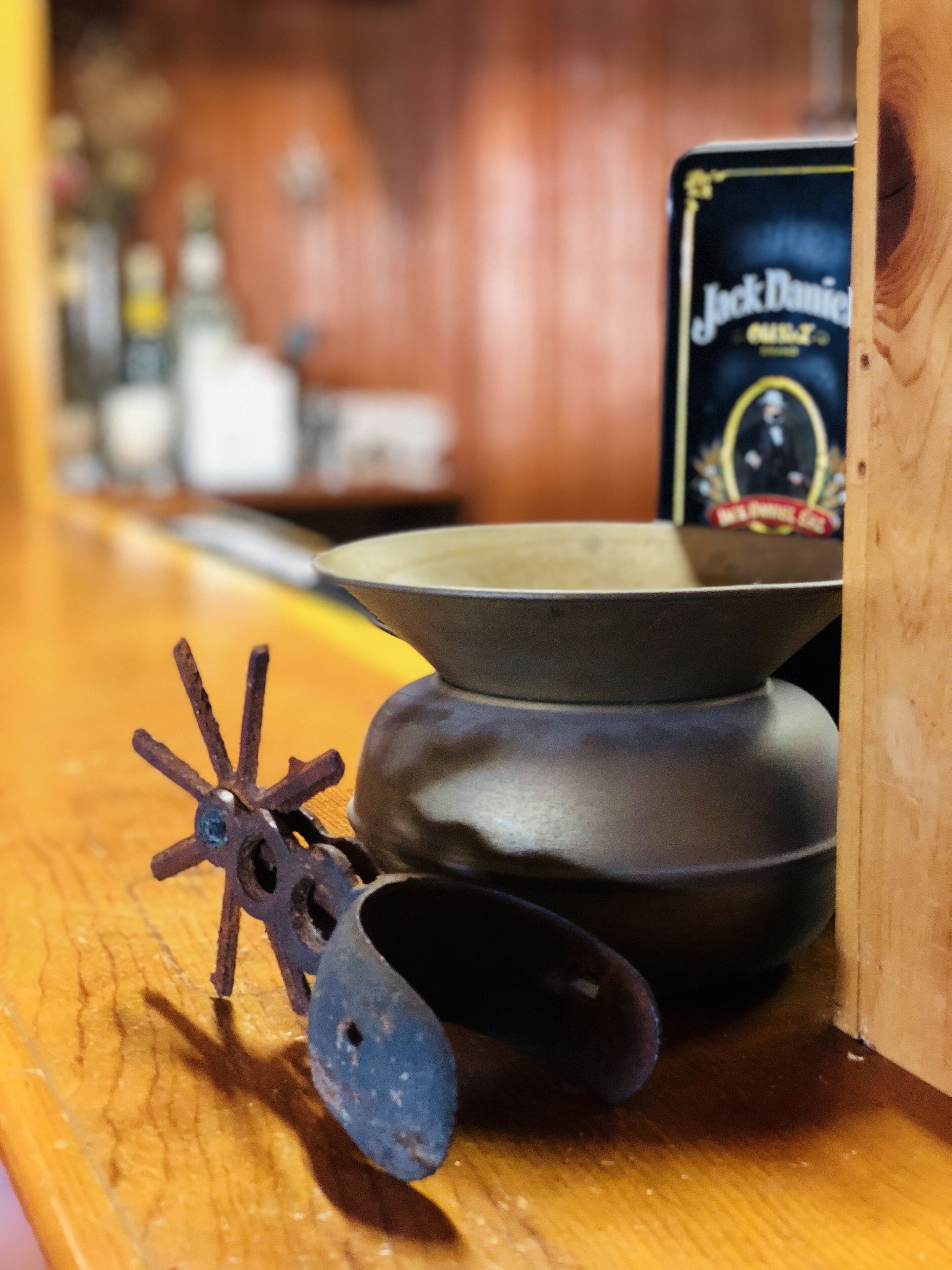 Un comptoir de bar en bois, agrémenté d’un pot en métal au style rustique et d’une bouteille de whisky Jack Daniel’s ancienne.