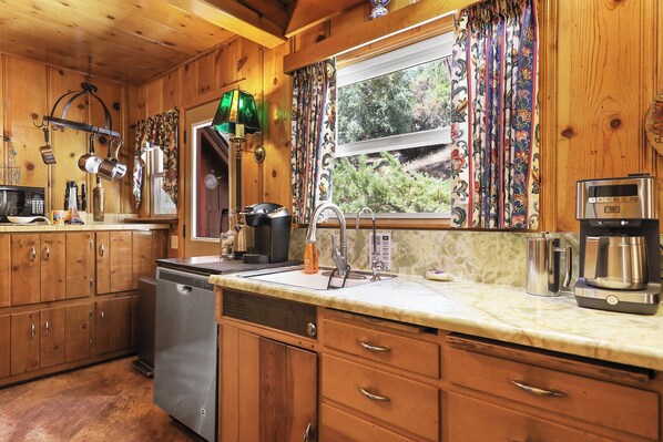 A kitchen with wooden cabinets, a dishwasher, a sink, and a window with curtains.