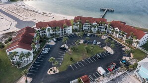 An aerial view of a coastal hotel with multiple buildings, a parking lot, and a beach.