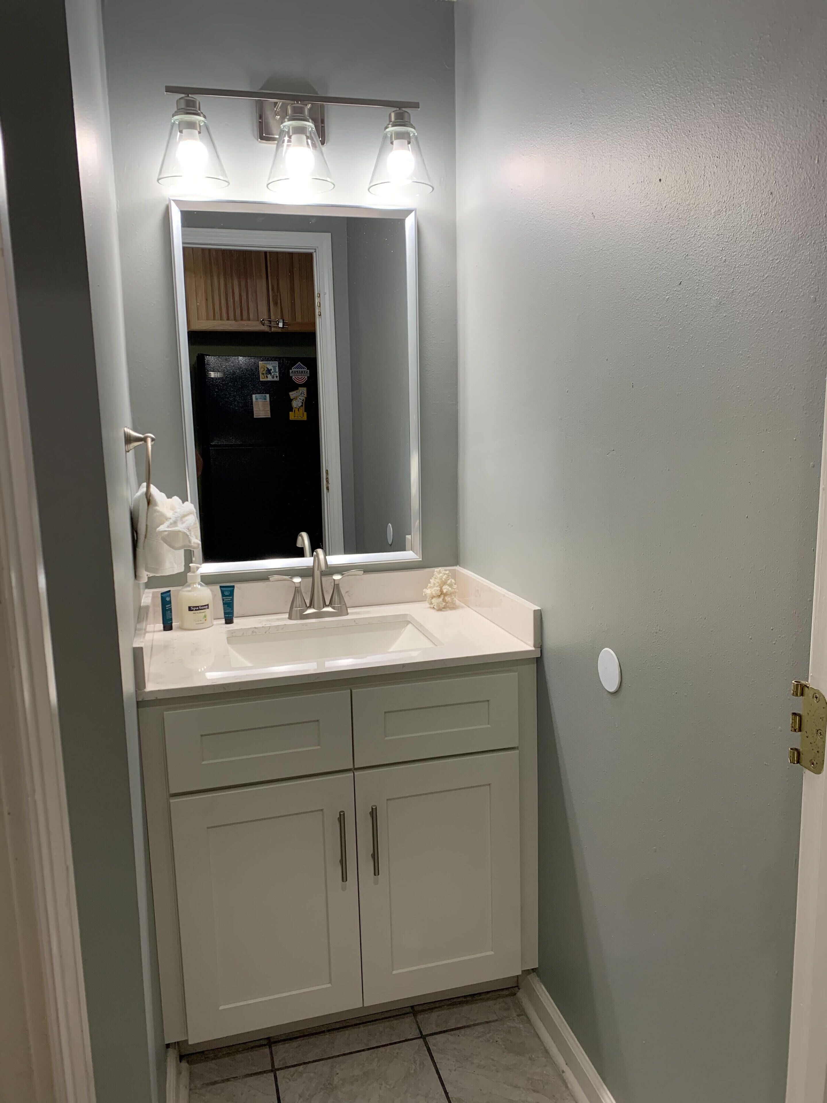 A bathroom with a white vanity, a mirror, and a sink. There are three light fixtures above the mirror.
