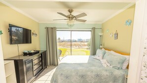 A bedroom with a bed, a desk, a ceiling fan, and a view of the outside.
