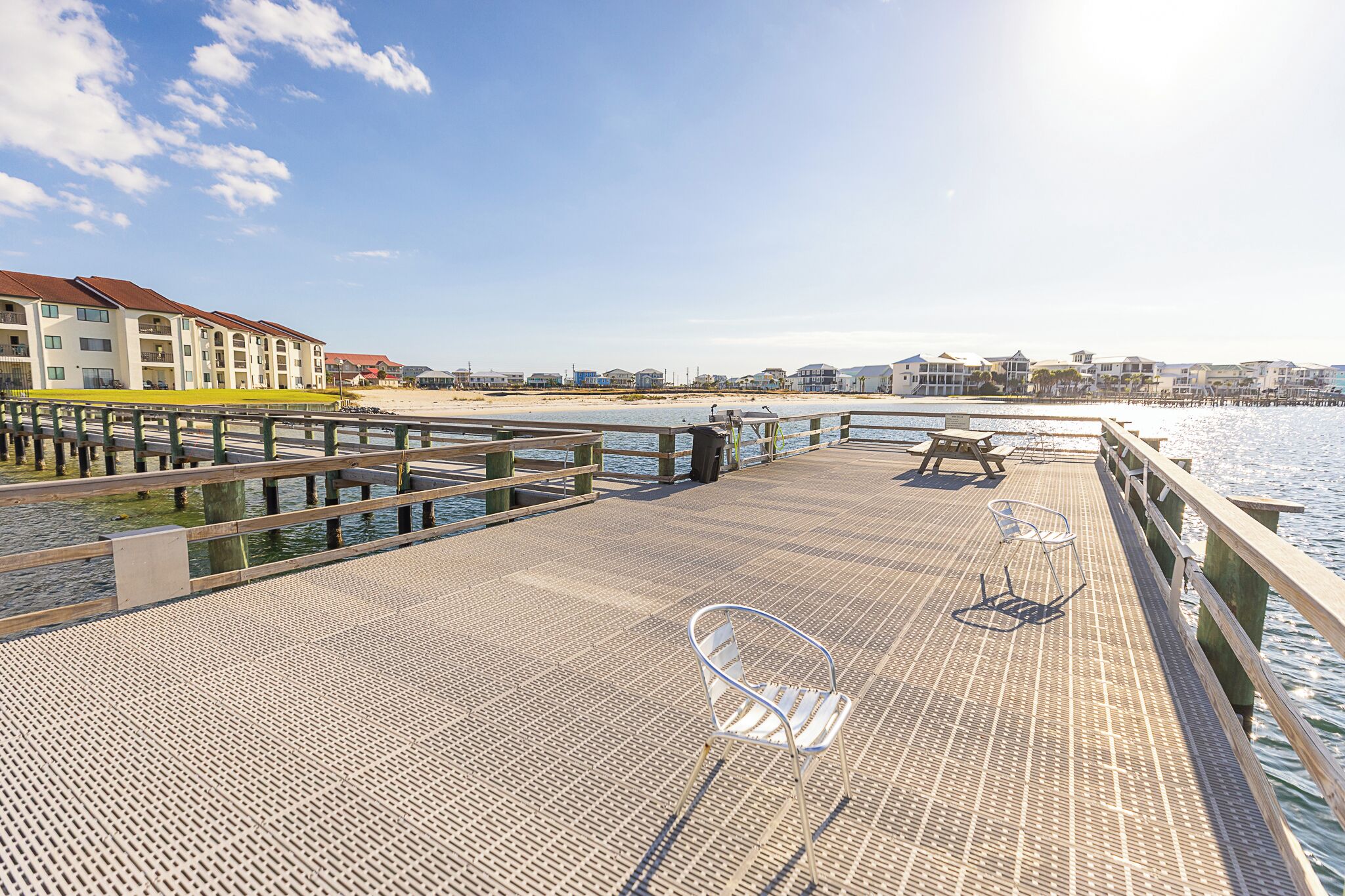 A wooden pier with metal chairs and a table, overlooking a beach and water.