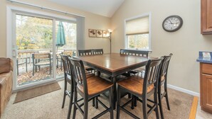 A dining area with a wooden table and chairs, a sliding glass door leading to an outdoor patio, and a clock on the wall.