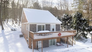 A cabin with a deck, a covered porch, and a snow-covered roof.