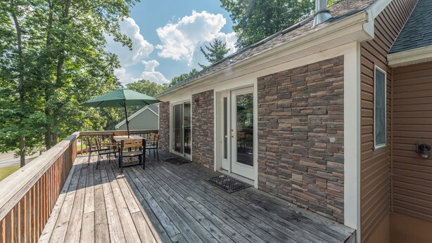 A wooden deck with a table and chairs, a green umbrella, and a stone exterior wall.