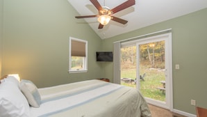 A bedroom with a bed, a ceiling fan, a TV, and a sliding glass door to a backyard.