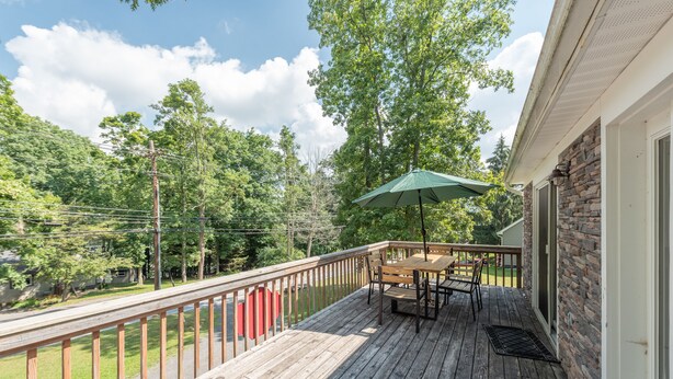 A wooden deck with a table and chairs, a green umbrella, and a stone wall.