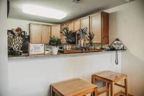 A kitchen with wooden cabinets, a countertop with various items, a sign that says "home sweet home", and a telephone on the wall.