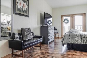 A bedroom with a bed, a dresser, a TV, a mirror, and a window with a wreath.