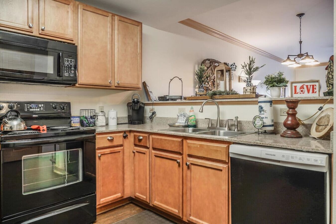 A kitchen with wooden cabinets, a microwave, stove, sink, and dishwasher.