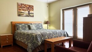 Une chambre à coucher avec un lit, une table de chevet, une lampe, une chaise et un tableau au mur.