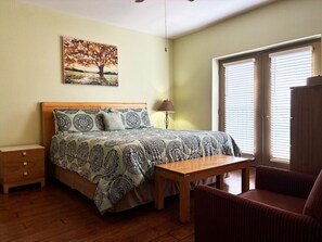 A bedroom with a bed, bedside table, lamp, chair, and a painting on the wall.