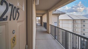 Un couloir avec un balcon, une porte portant l’inscription « 2705 », et une vue sur des immeubles d’habitation.