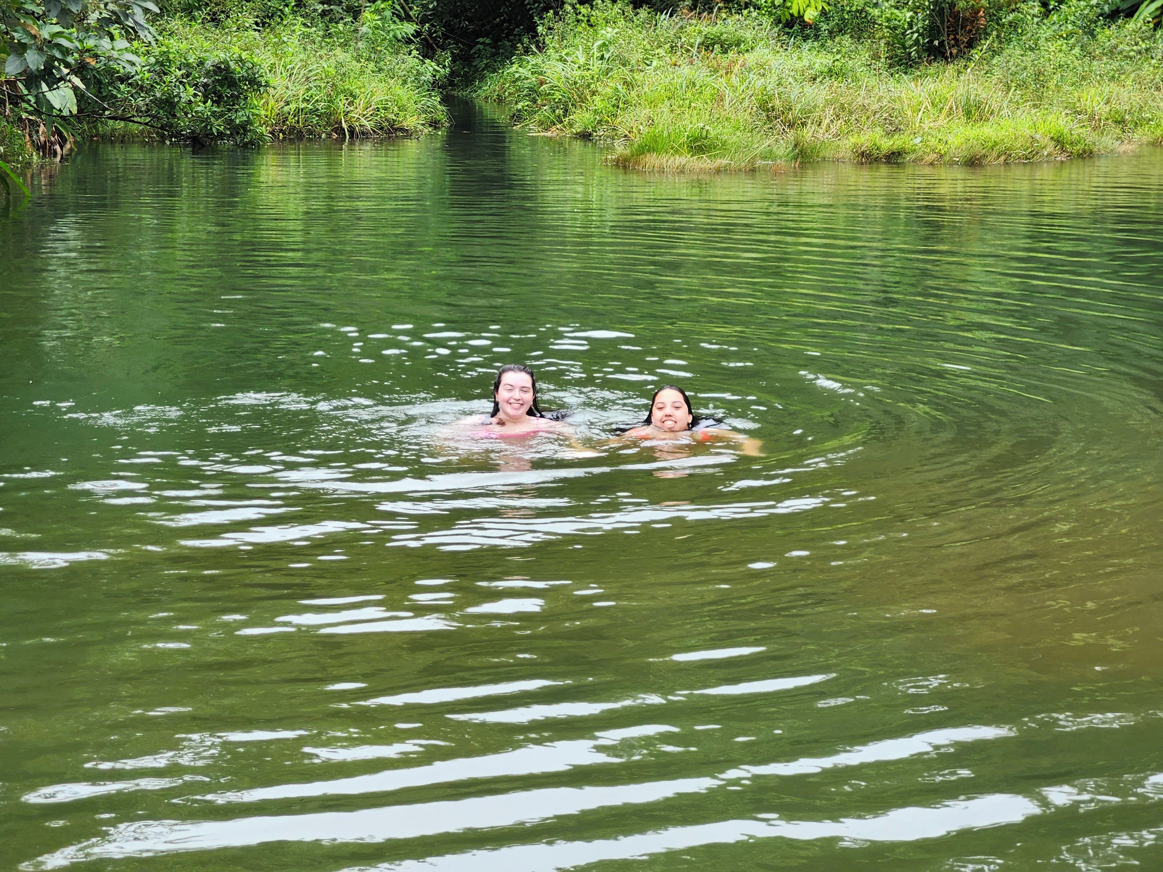 Two people swimming in a body of water surrounded by greenery.