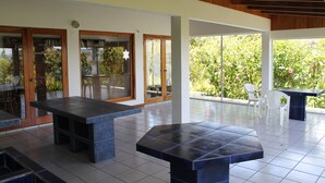 Ein großzügiger Patio-Bereich mit einem großen Tisch und Stühlen, einer Holzbeschichtung an der Decke und großen Fenstern mit Blick auf Grünflächen.