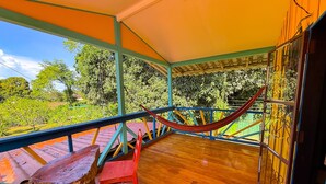 Una terraza de madera con una hamaca, una silla roja y una mesa de madera.