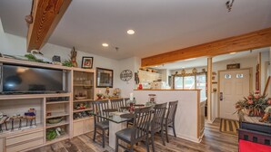 A spacious living area with a glass dining table, wooden chairs, and a television on a shelf.