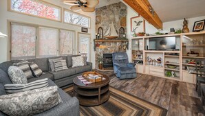 A cozy living room with a stone fireplace, a comfortable sofa, a wooden coffee table, and a television on a wooden stand.