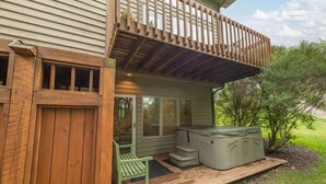 A deck with a hot tub, a wooden bench, and a covered patio area.