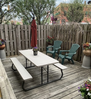 A wooden deck with a picnic table and two green chairs.