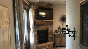 A living room with a stone fireplace, a flat-screen TV, and a chandelier.