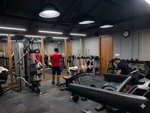 Une salle de sport équipée de matériel d’exercice, de miroirs et d’une horloge au mur.
