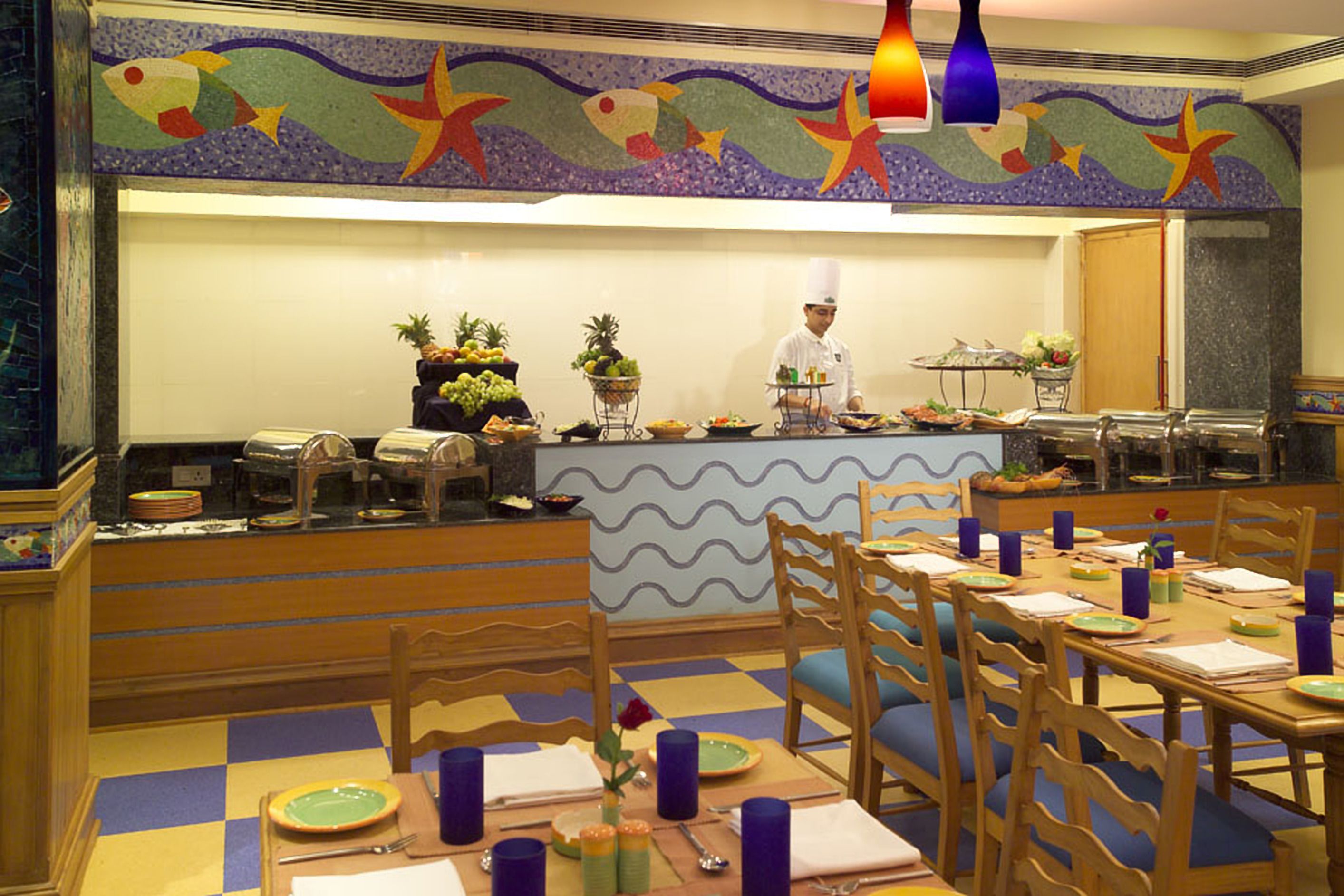 A restaurant with a chef at the counter, wooden chairs, and a checkered floor.